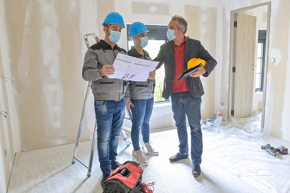 Trois professionnels du b&acirc;timent en r&eacute;union de chantier dans un espace en r&eacute;novation