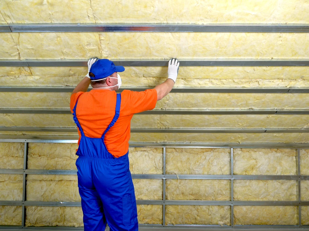 Ouvrier en combinaison bleue et t-shirt orange installant de l'isolation thermique sur mur intérieur