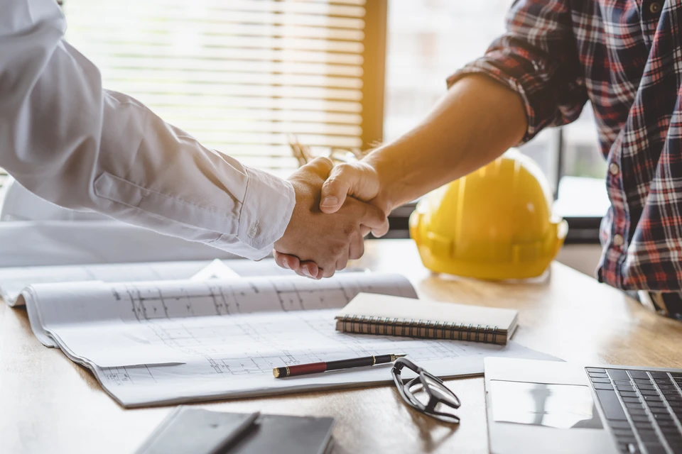 Le client serre la main de l'entrepreneur après avoir confirmé le plan de rénovation de la maison