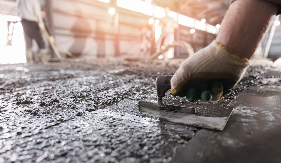Ouvrier réalisant le lissage d'une dalle de béton frais en extérieur avec une taloche métallique