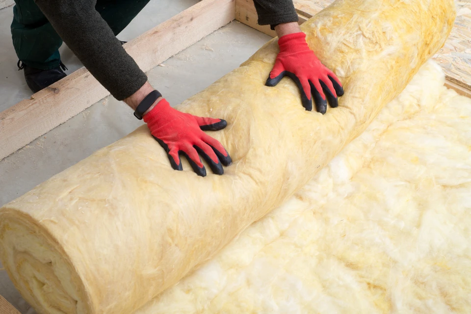 Ouvrier en bâtiment installant de l'isolant thermique en laine minérale jaune entre les montants d'une cloison intérieure